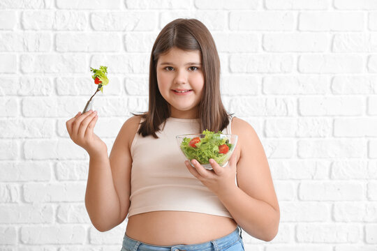 Overweight girl eating healthy vegetable salad on white brick background