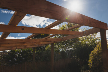 under construction garden pergola with wooden structure in sunny backyard surrounded by tropical...