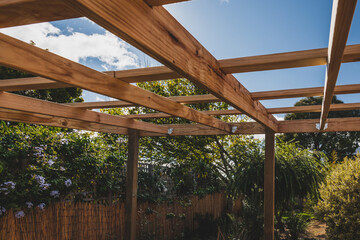 under construction garden pergola with wooden structure in sunny backyard surrounded by tropical plants - obrazy, fototapety, plakaty