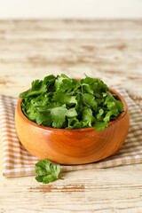 Bowl with fresh cilantro on light wooden background