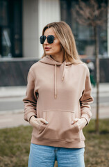 Fasion blonde woman in brown oversize hoodie, glasses and blue jeans, mockup for logo or branding...