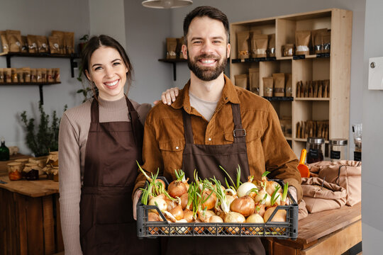 Smiling sellers man and woman holding basket with onion in local eco shop