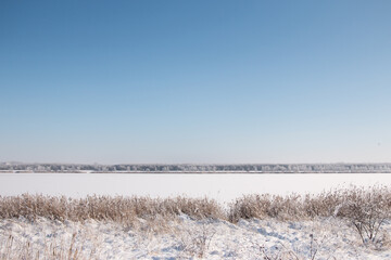 Winterlandschaft eines Sees bedeckt mit Eis und Schnee unter blauem, wolkenlosem Himmel
