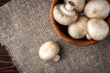 Champignon mushrooms in wooden bowl on dark wooden background.