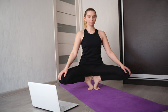 Young Woman Doing Asana At Home On Yoga Mat In Front Of Laptop