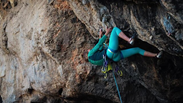 strong woman rock climber climbs hard tough rock route on very overhanging black cliff in Turkey. climber puts quickdraw and clips rope