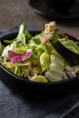 Caesar salad in the black plate on cocnrete background made with different lettuce, croutons, parmesan and chicken