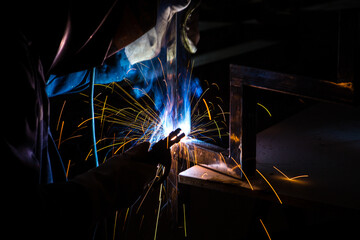 A man welder with construction gloves and a welding mask is welded with a welding machine metal in...