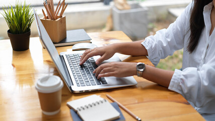 Female hands working with laptop computer on wooden desk with stationery in cafe