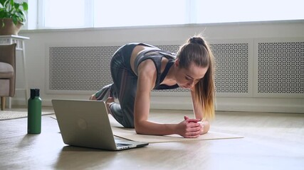 Woman practices yoga on floor at home room, trains and uses laptop spbas.