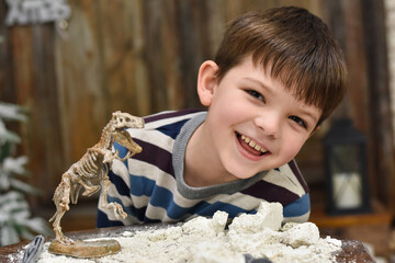 Happy child digging the dinosaur and having fun with archaeology excavation kit. Boy plays an...