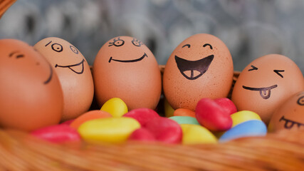 Stack of eggs with hand drawn faces on straw basket with colorful candy, easter preparation,...