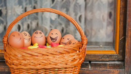Stack of eggs with hand drawn faces on straw basket with colorful candy, easter preparation,...