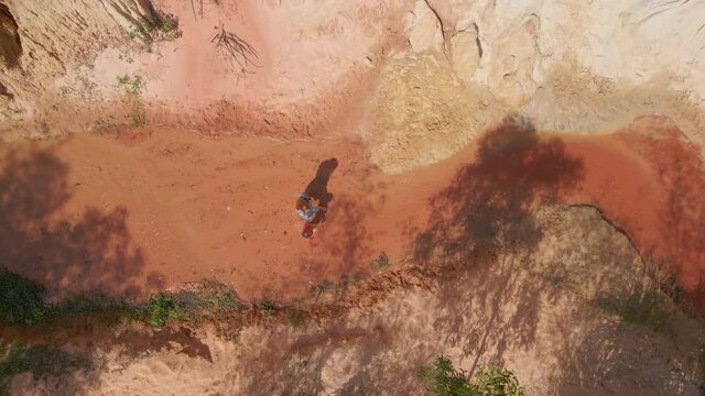 Aerial slowmotion shot. A woman and her son walk along a red canyon or Fairy stream at the border of desert in the Mui Ne village in southern Vietnam