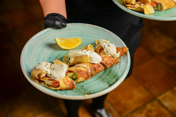 Savory crepe rolls with meat and vegetable filling served with sour cream by waiter in restaurant or diner.