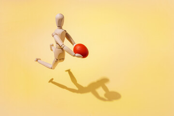 A wooden doll holds a red egg in its hands as it hovers over a yellow background