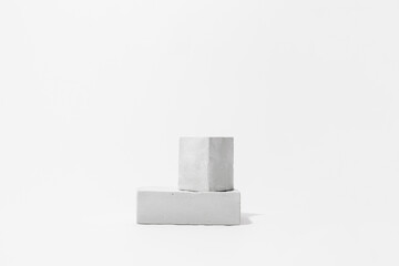 Gray cocncrete cube and parallelepiped shaped pedestals on white background with copy space, side view. Podium mockup for products. Advertising template. Stone platform. Abstract geometric pedestal.