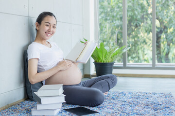 Pregnant mothers are reading books. Happy pregnant asian woman reading book on carpet at home.