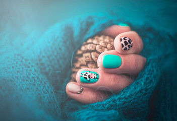 Handmade creative manicure design with farm animal motives. Cow hair texture on the nails. Summer style. Selective focus on a drawn cow, blurred background, pine cone and knitted sweater.