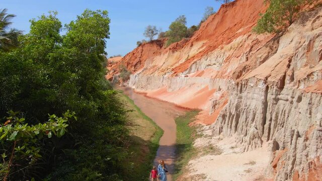 Aerial slowmotion shot. A woman and her son walk along a red canyon or Fairy stream at the border of desert in the Mui Ne village in southern Vietnam