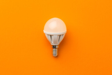 Light bulb on bright orange background top view