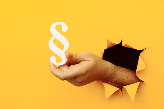 Male hand holds a paragraph as a sign of justice and law through a yellow paper hole