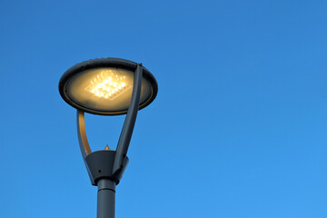 Led lamp glowing on blue sky background. Electric lighting, energy-saving street lantern