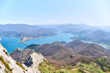 Fototapeta na wymiar Aerial view from the Gilbo peak towards the Riaño reservoir, the village and the Picos de Europa. Snow on top of the mountains. Spring in León