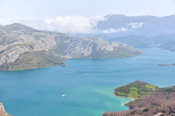 Aerial view of the Riaño reservoir with a boat sailing its turquoise blue waters surrounded by mountains in spring.