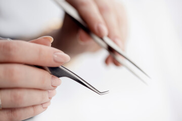 Close-up hand of master holds tools for eyebrow correction and eyelash extension tweezers and tongs on white background