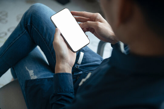 Mockup image blank white screen moblie phone. Closeup hand holding texting using mobile relax on sofa at home from behind. people contact marketing business and technology