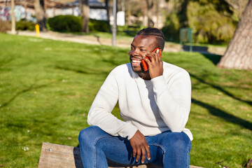 Young African American man talking on cell phone in a park. Black man with braids in his hair. 