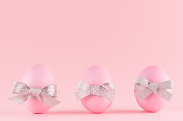 Pink easter eggs with grey bows standing in row on pastel pink background.