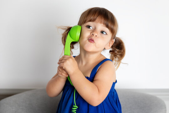 Cute little girl blowing kiss while talking on green corded phone