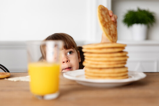 Young girl peeking behind kitchen table stealing a pancake