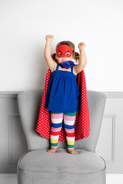 Funny toddler girl dressed as superhero standing on chair