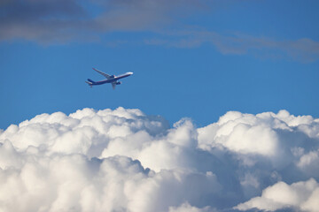 Airplane flying in the blue sky above the white clouds. Commercial plane at flight, travel concept