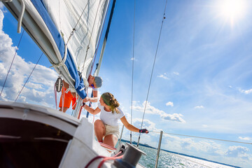 Young woman and man sailing on a yacht. Sailboat crewmember trimming main sail during sail on vacation in summer season - obrazy, fototapety, plakaty