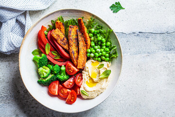 Vegan salad bowl with sweet potatoes, broccoli, tomato, peas and hummus.