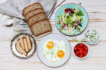 Plate with fried eggs, bread, salad, sausages and cottage cheese on brown wooden table