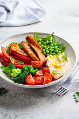 Vegan salad bowl with sweet potatoes, broccoli, tomato, peas and hummus.