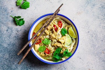Thai green curry noodles with chicken, chili and cilantro in white bowl.