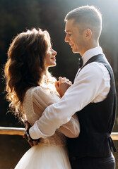 Loving young couple looking into each other's eyes, standing hand in hand together on a pier near a mountain lake