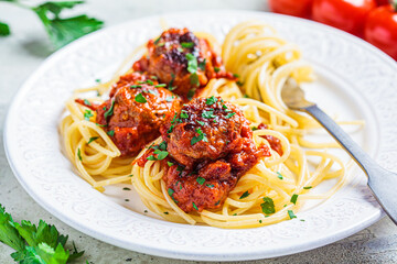 Spaghetti pasta with meatballs in tomato sauce and herbs on white plate, close up. Comfort food concept.