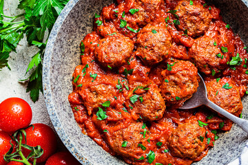 Fried meatballs with tomato sauce and parsley in  pan, top view.