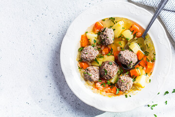 Homemade meatballs soup with vegetables in white plate, gray background, top view, copy space.