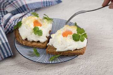 A woman's hand holds a fork over an Orsini diet dish of beaten and baked eggs . Light background. French aristocrats ' breakfast