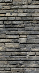 big dark wall with black and gray irregular bricks of stone - vertical background texture	