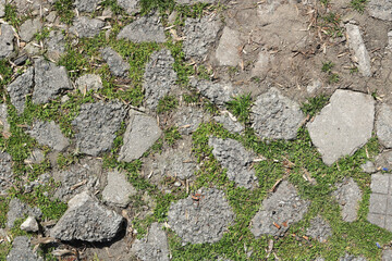 old cracked and weathered broken floor of cement, stone and sand, with grass and moss growing - rough texture background