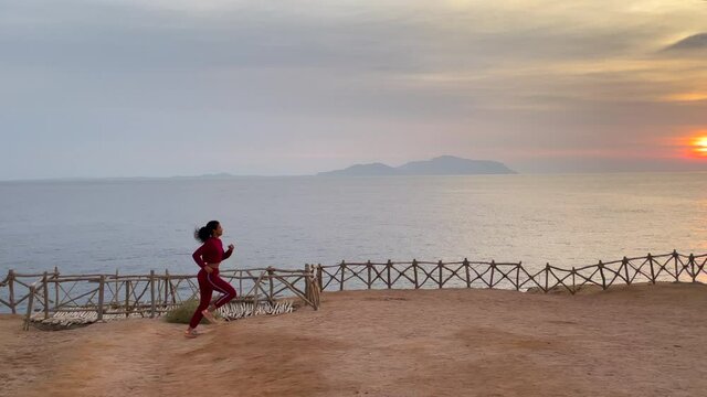 Boost your health. Motivated young woman admiring the seascape while jogging along the cliff edge at sunrise. Slow motion. Body positive, healthy lifestyle, nature concept. Side view. Full length